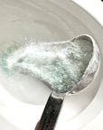 Scoop of etee probiotic toilet bowl cleaner powder being poured into white toilet bowl
