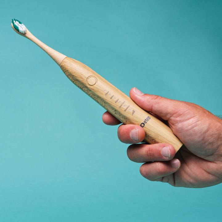 electric toothbrush with bamboo head being held by a man's hand