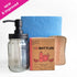 Set of cleaning supplies including a glass bottle with pump, citrus-scented powdered dish soap in recyclable box, scourer, and reusable paper towel
