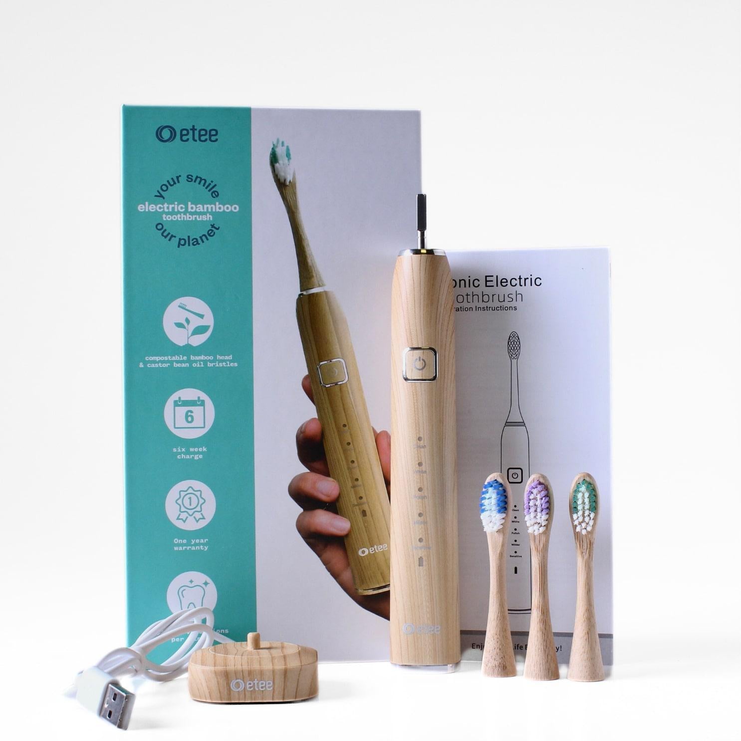 etee electric toothbrush with replaceable bamboo head standing up with three toothbrush heads and stand, in front of box