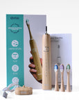 etee electric toothbrush with replaceable bamboo head standing up with three toothbrush heads and stand, in front of box
