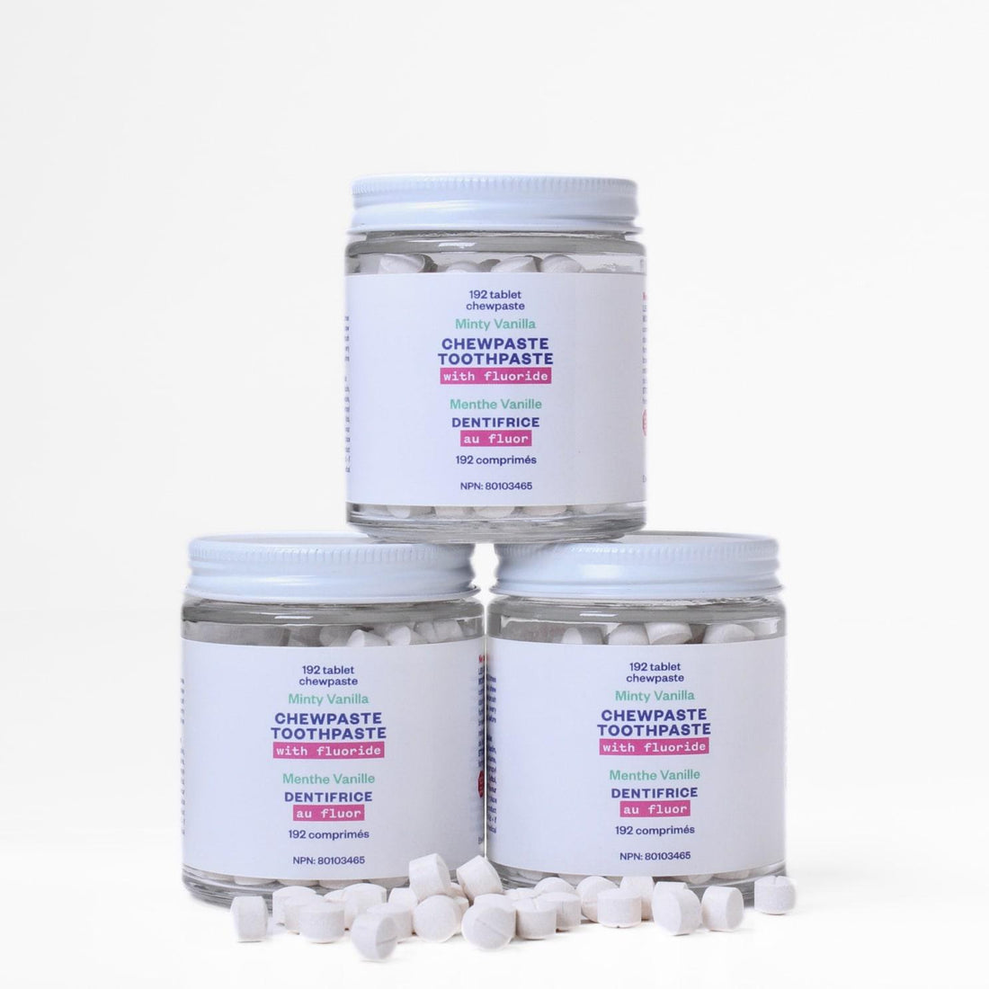 Three tubs of etee fluoride chewpaste stacked on top of each other with about 20 chewpaste tablets strewn in front of the jars