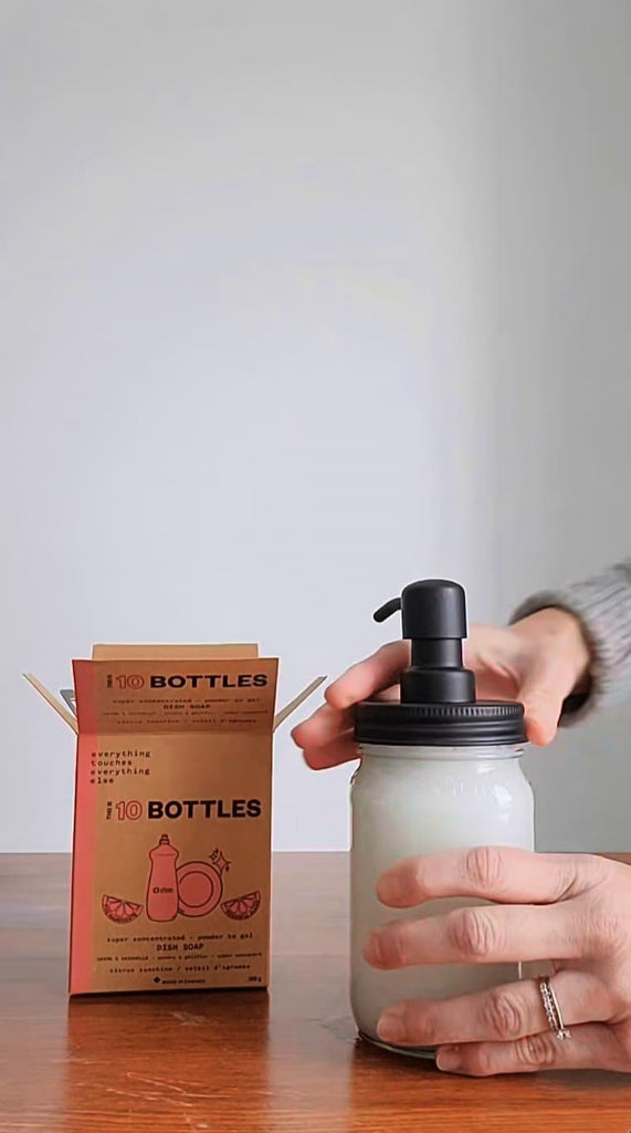 A spoonful of dish soap powder is placed into a glass jar with water in it. A woman then stirs the dish soap until it becomes sudsy and then she puts the mason jar lid with a pump on top.