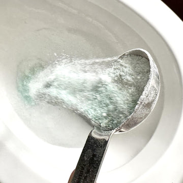Scoop of etee probiotic toilet bowl cleaner powder being poured into white toilet bowl